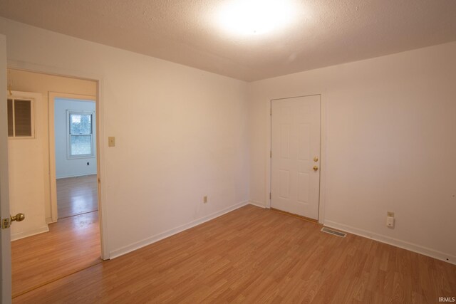 empty room with light wood finished floors, visible vents, a textured ceiling, and baseboards