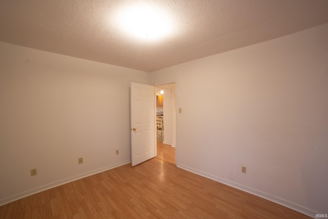 unfurnished room with light wood-style flooring, a textured ceiling, and baseboards