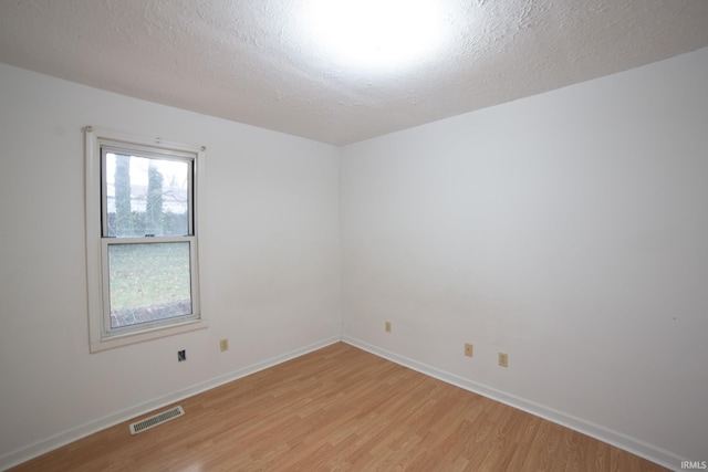 empty room with visible vents, a textured ceiling, light wood-type flooring, and baseboards