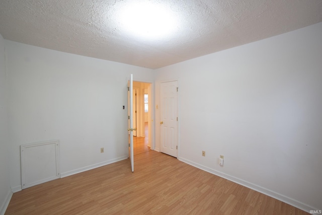 spare room featuring light wood-style flooring, a textured ceiling, and baseboards