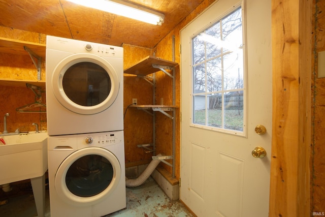 clothes washing area with a sink, stacked washer and dryer, and laundry area