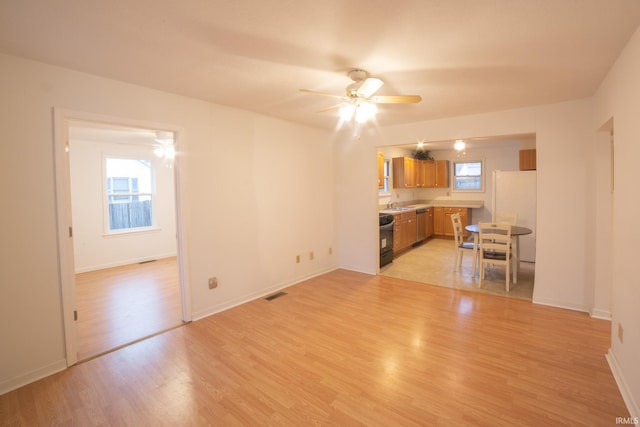 unfurnished living room with visible vents, baseboards, light wood-style floors, a ceiling fan, and a sink