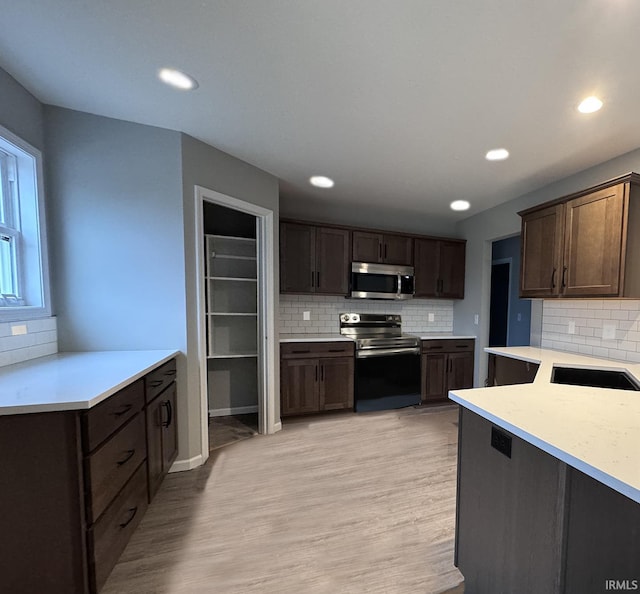 kitchen with appliances with stainless steel finishes, light wood-type flooring, tasteful backsplash, and dark brown cabinetry