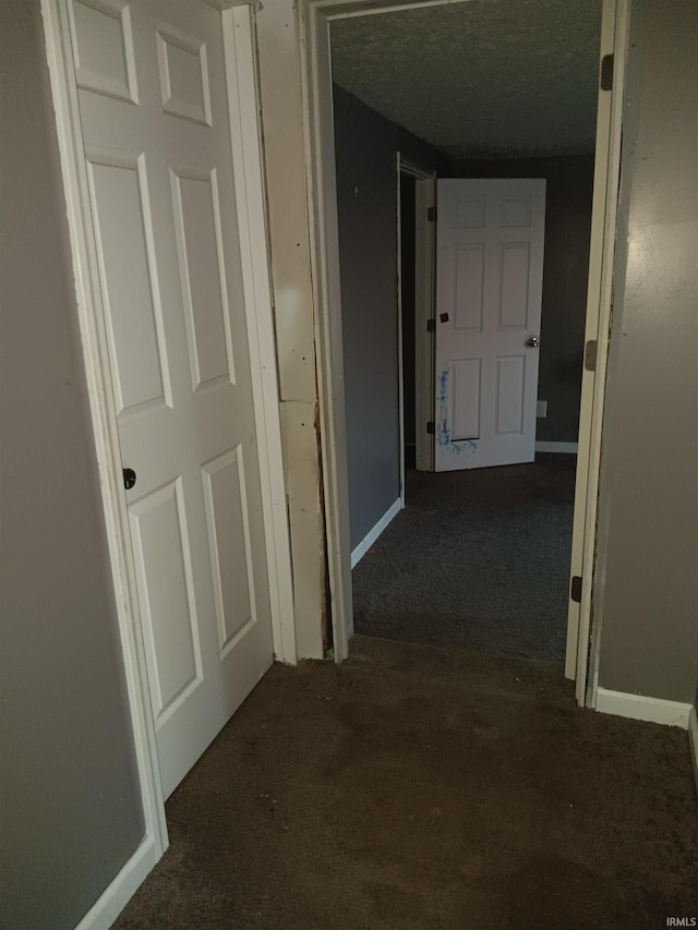 corridor with dark carpet and a textured ceiling