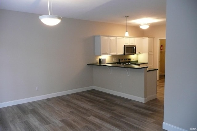 kitchen with hanging light fixtures, dark hardwood / wood-style flooring, kitchen peninsula, white cabinets, and appliances with stainless steel finishes