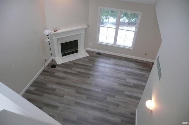 unfurnished living room with a tiled fireplace and dark hardwood / wood-style flooring