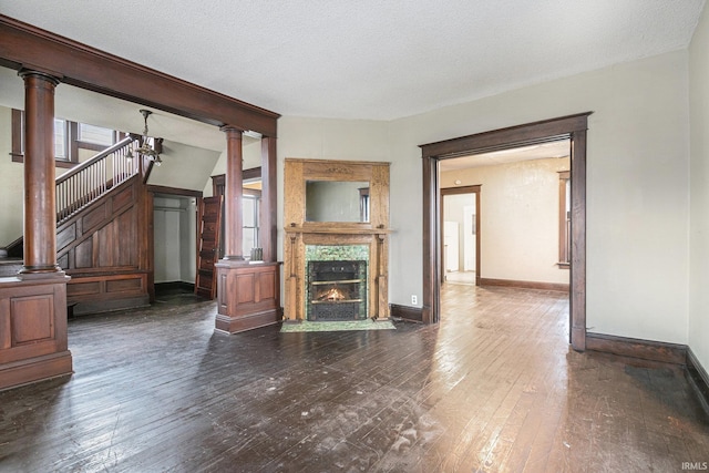 unfurnished living room featuring decorative columns, dark hardwood / wood-style flooring, a high end fireplace, and a textured ceiling