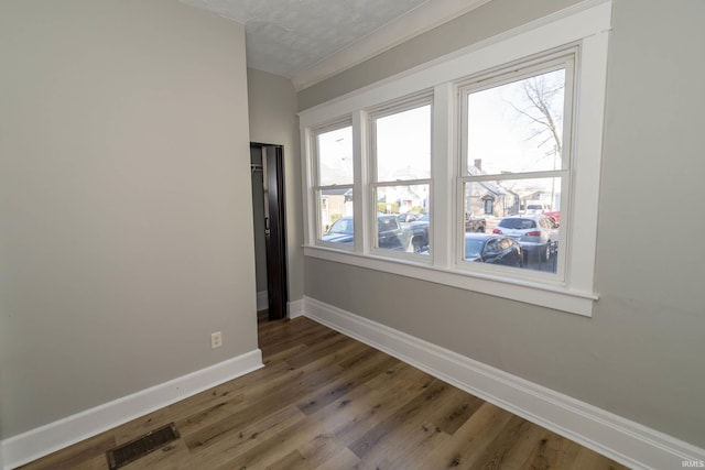 spare room with dark wood-type flooring, a textured ceiling, and ornamental molding