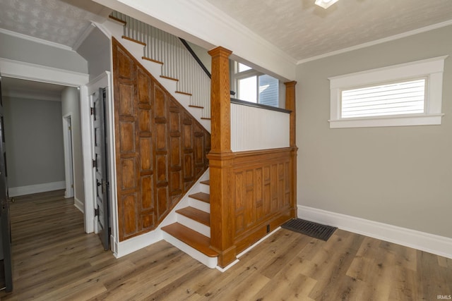 staircase featuring ornate columns, crown molding, a textured ceiling, and hardwood / wood-style flooring