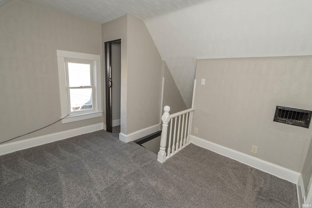 additional living space with a textured ceiling, dark carpet, and lofted ceiling