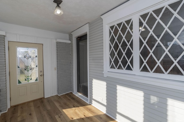 entryway with wood-type flooring, a textured ceiling, and brick wall