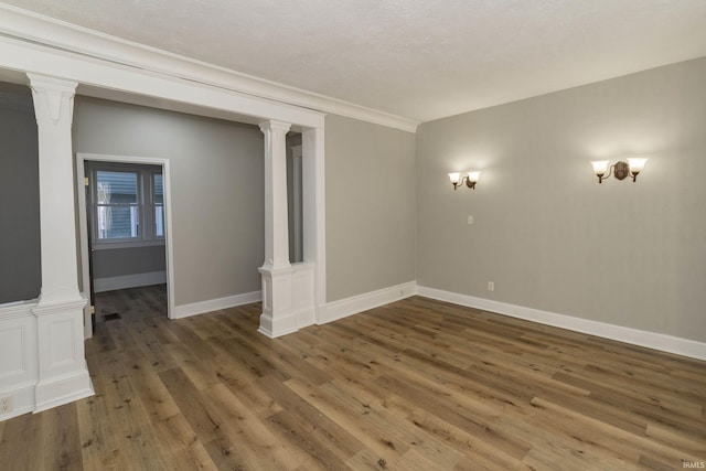 spare room featuring ornate columns, dark wood-type flooring, and a textured ceiling