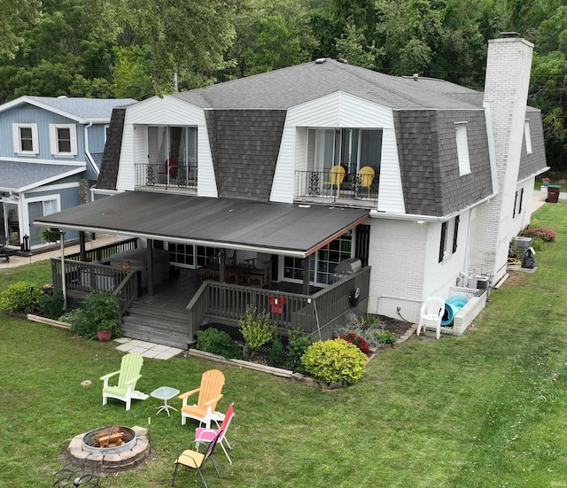 back of house with a balcony, a yard, and an outdoor fire pit