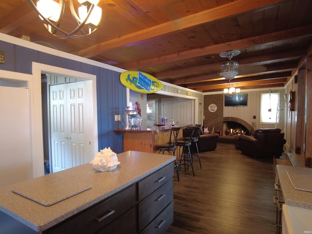 kitchen featuring wooden ceiling, ceiling fan with notable chandelier, a brick fireplace, beamed ceiling, and dark hardwood / wood-style flooring