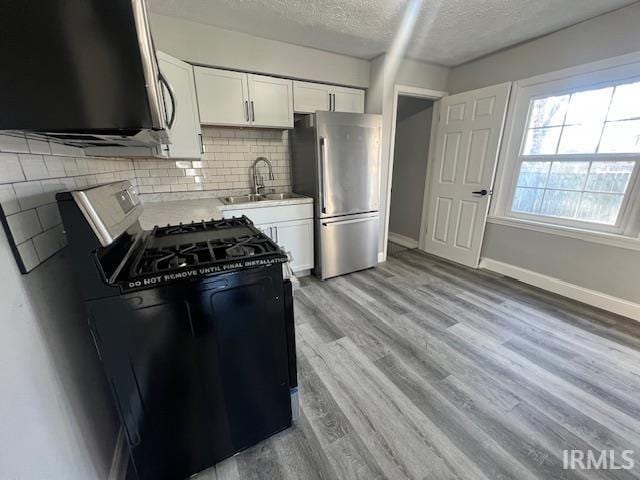 kitchen with stainless steel fridge, white cabinetry, black range oven, and sink