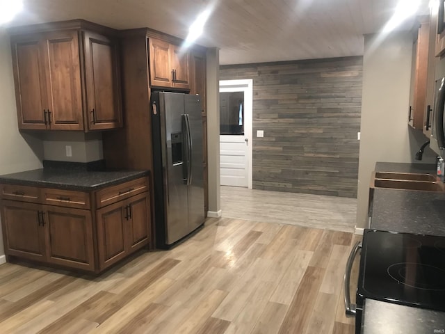 kitchen featuring wood walls, black stove, sink, stainless steel fridge, and light wood-type flooring