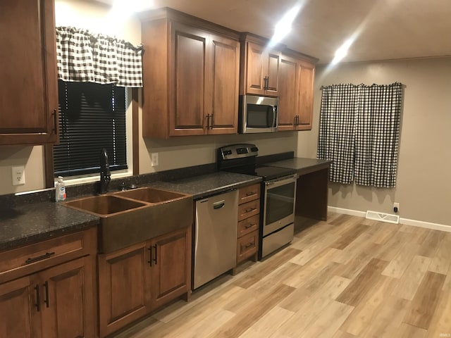 kitchen with appliances with stainless steel finishes, light wood-type flooring, dark stone countertops, and sink