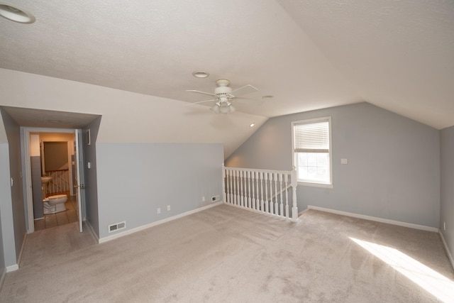 additional living space featuring a textured ceiling, ceiling fan, light colored carpet, and vaulted ceiling