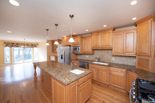 kitchen with stainless steel appliances, a kitchen island with sink, sink, pendant lighting, and light hardwood / wood-style floors