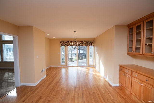 unfurnished dining area featuring a chandelier, light wood-type flooring, and a healthy amount of sunlight