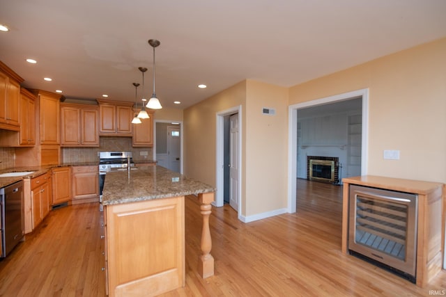 kitchen featuring tasteful backsplash, a kitchen island with sink, beverage cooler, and light hardwood / wood-style floors