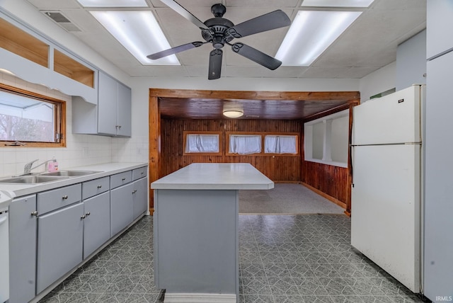 kitchen featuring a center island, sink, tasteful backsplash, white refrigerator, and wooden walls