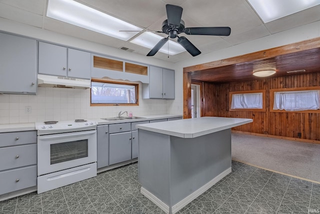 kitchen with wood walls, white range with electric cooktop, sink, decorative backsplash, and a kitchen island