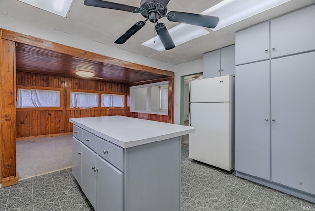 kitchen with wooden walls, a center island, white fridge, and ceiling fan