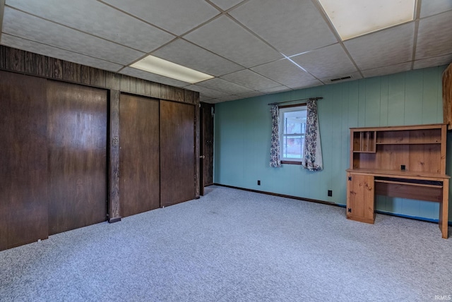 basement with light carpet, a drop ceiling, and wood walls