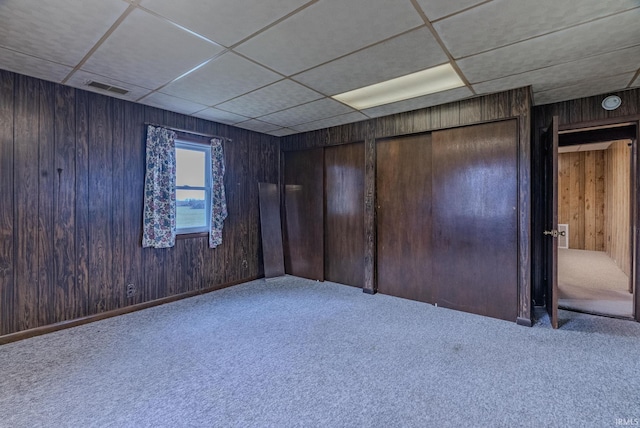 carpeted spare room featuring wood walls and a drop ceiling