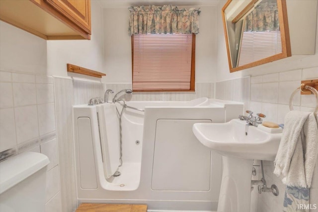 bathroom with a tub, tile walls, and toilet