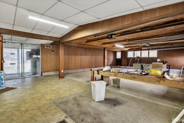 basement featuring a drop ceiling and wooden walls