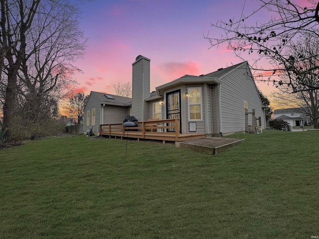 back house at dusk featuring a wooden deck and a yard