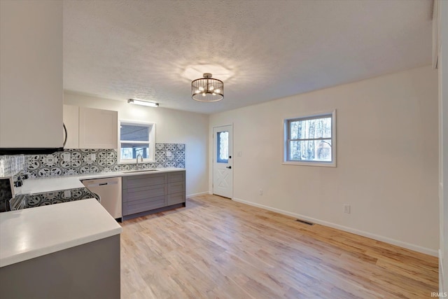 kitchen featuring gray cabinetry, dishwasher, tasteful backsplash, light hardwood / wood-style flooring, and white stove