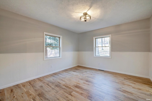 unfurnished room with a healthy amount of sunlight, a textured ceiling, and light wood-type flooring