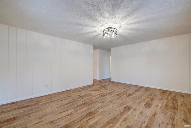 interior space with a textured ceiling, light wood-type flooring, and wooden walls