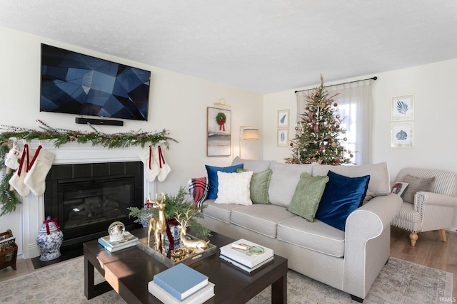 living room featuring a tiled fireplace, a textured ceiling, and light wood-type flooring