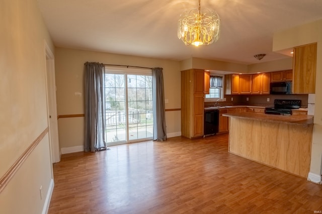 kitchen with light wood-type flooring, an inviting chandelier, a healthy amount of sunlight, and black appliances