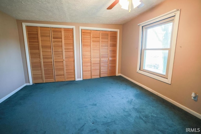 unfurnished bedroom featuring a textured ceiling, ceiling fan, two closets, and dark colored carpet