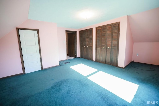 unfurnished bedroom featuring carpet, vaulted ceiling, and multiple closets