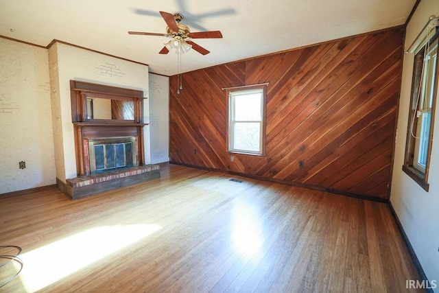 unfurnished living room with a brick fireplace, wood walls, ceiling fan, and hardwood / wood-style flooring