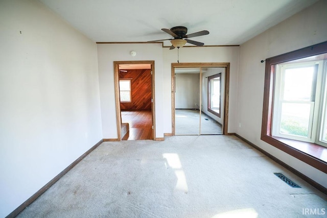 carpeted empty room with a wealth of natural light, ceiling fan, and wood walls