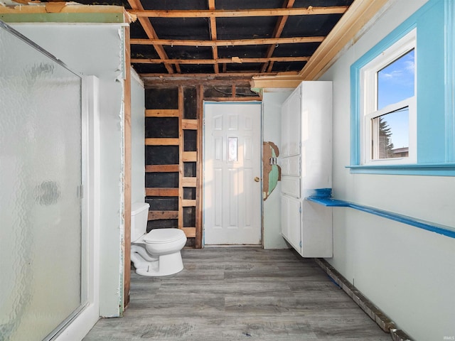 bathroom with hardwood / wood-style flooring, toilet, and a shower with door