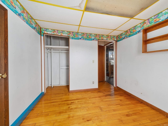 unfurnished bedroom featuring a closet, a drop ceiling, and light wood-type flooring