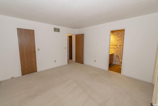 unfurnished bedroom featuring light carpet, a textured ceiling, ensuite bath, and a closet