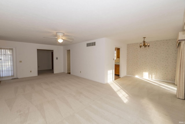 carpeted spare room featuring ceiling fan with notable chandelier