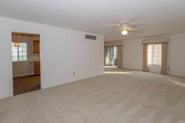 unfurnished room featuring light carpet, ceiling fan with notable chandelier, and plenty of natural light