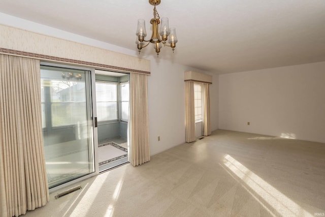 carpeted empty room with an inviting chandelier