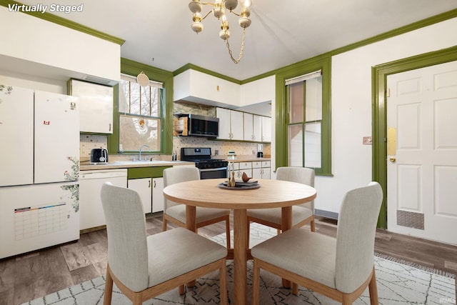 dining area featuring sink, light hardwood / wood-style flooring, a notable chandelier, and crown molding