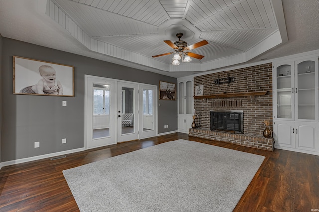 unfurnished living room featuring a brick fireplace, a raised ceiling, ceiling fan, wooden ceiling, and dark hardwood / wood-style floors